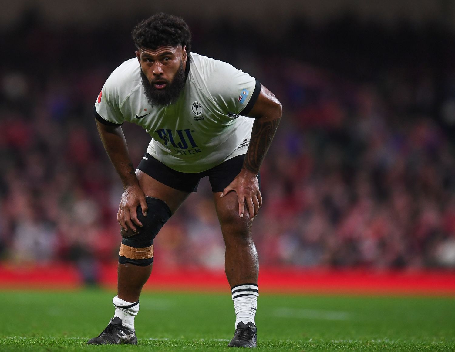 Rugby player in white uniform bends forward in ready position during match.