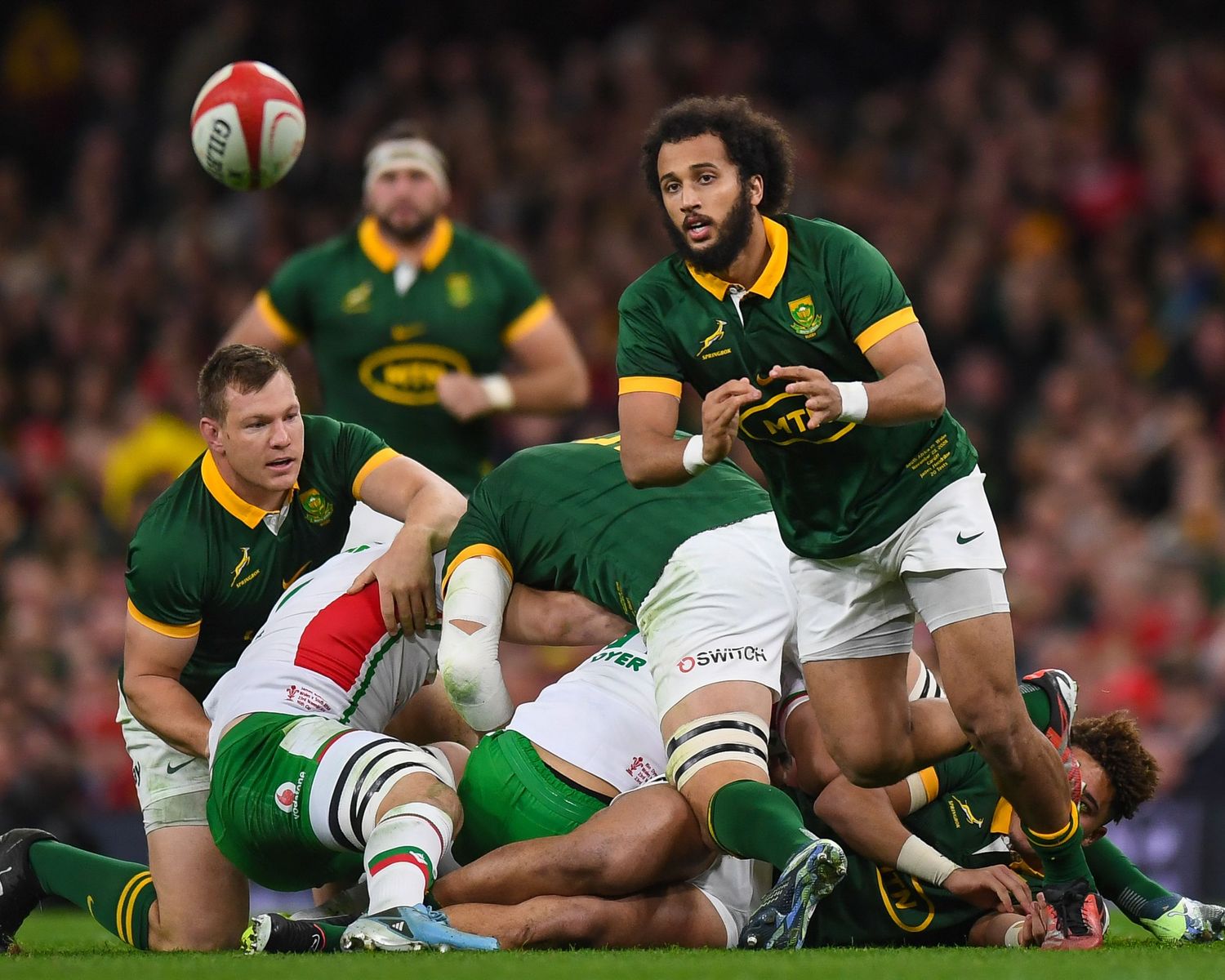 Rugby players in green South African jerseys compete for possession during an intense match against players in white.