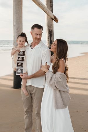 Family embraces lovingly on a serene beach with wooden posts and soft lighting at sunset.