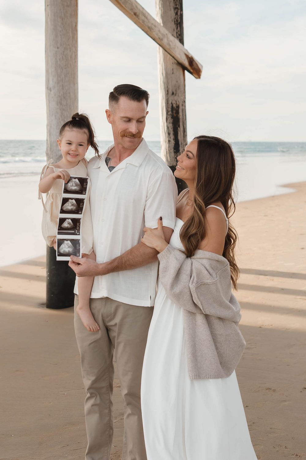 Family embraces lovingly on a serene beach with wooden posts and soft lighting at sunset.