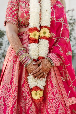 Close-up details of traditional Indian bridal attire showing red lehenga, white floral garlands, and henna-adorned hands.