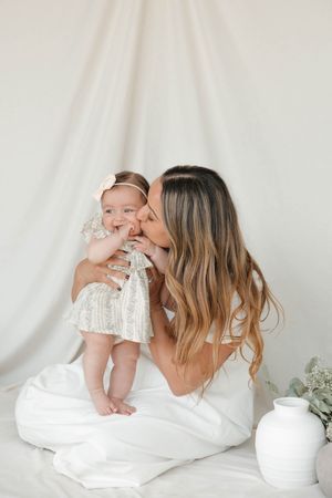 A tender moment between parent and baby in white outfits against a light background with minimal decor.