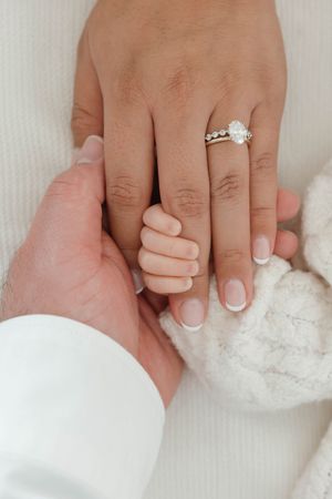 Close-up view of hands wearing a sparkling engagement ring against white fluffy fabric.