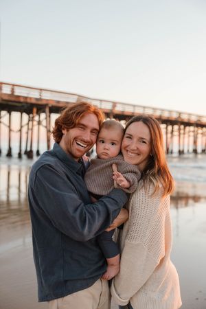 Family shares joyful moments together at sunset on a beach near a wooden pier.