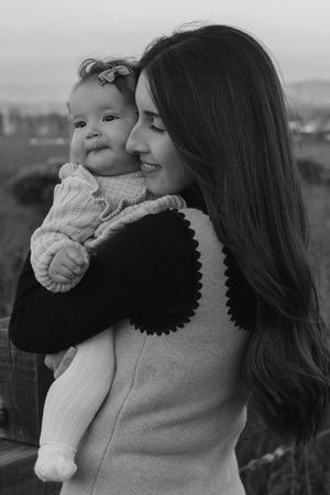 A tender black and white photo series showing a parent holding and kissing a small baby in a knit sweater.