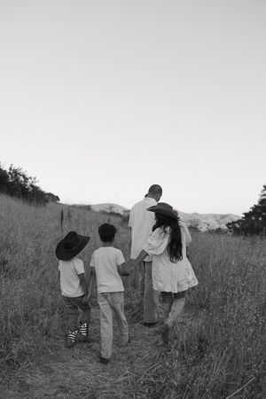 Black and white photo of a family of four walking through a grassy field path, two children wearing cowboy hats.
