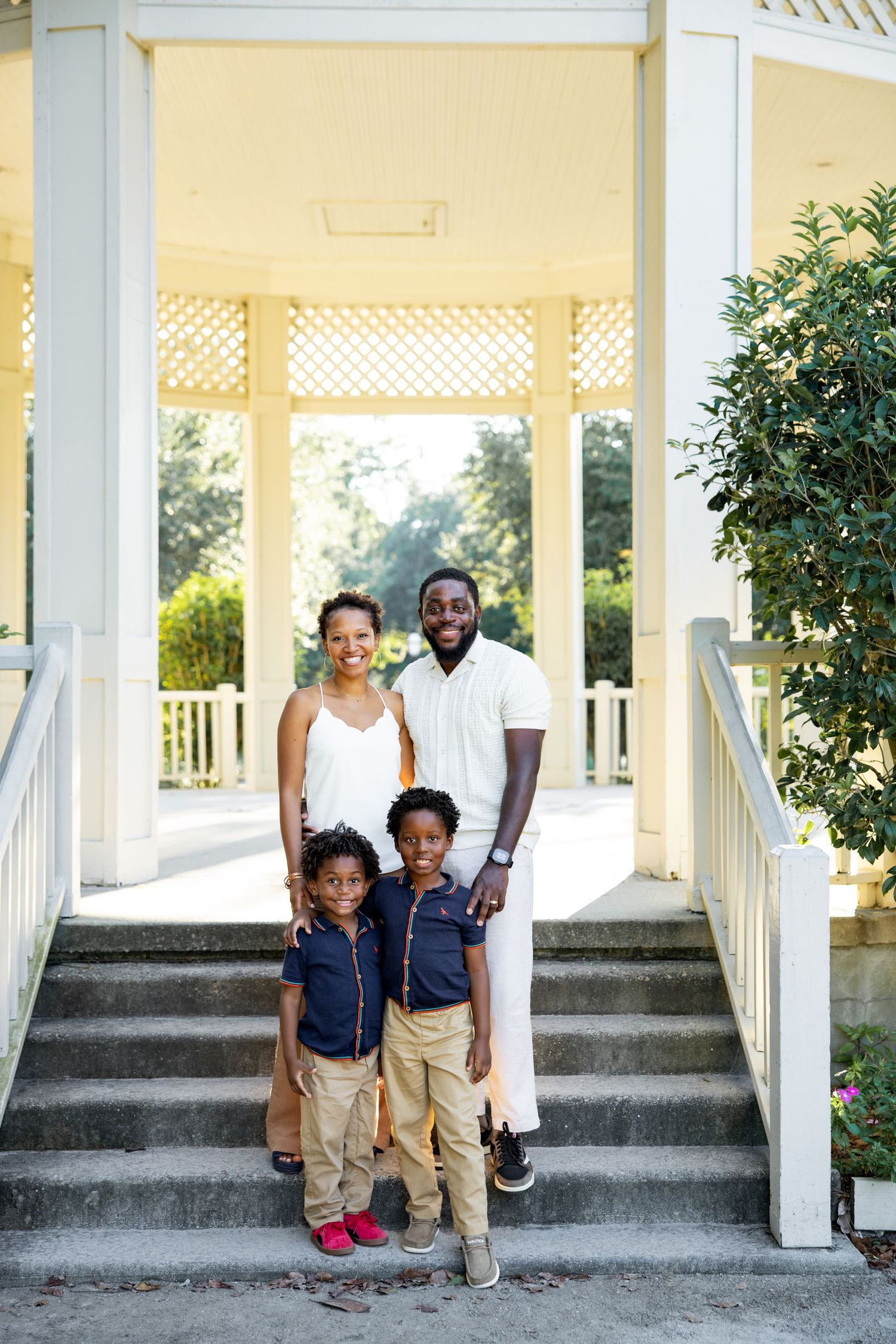 Family poses together on white gazebo steps in matching navy and khaki outfits during outdoor photo session.