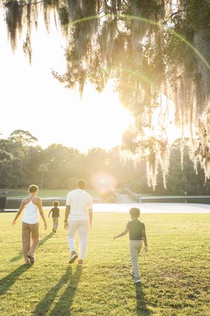 Silhouettes of people playing and running in a grassy field during golden hour with Spanish moss in trees.