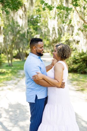 A couple shares an intimate moment while embracing on a scenic path with Spanish moss.