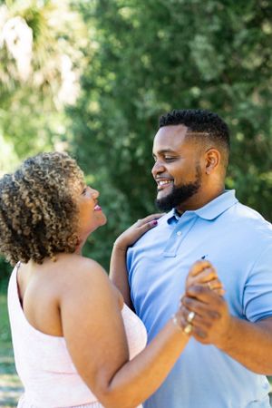 A couple laughs together during a dance moment in a sunny outdoor setting.