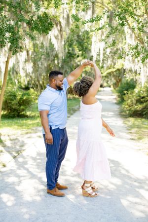 A couple dancing together on a sunlit path surrounded by Spanish moss hanging from trees in a romantic setting.