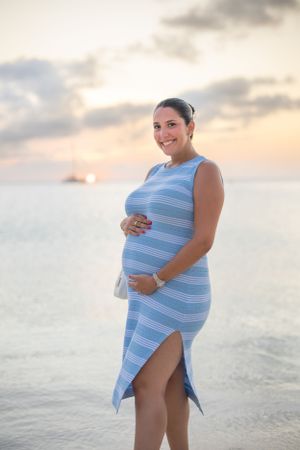 Maternity beach photo at sunset wearing a blue striped dress.