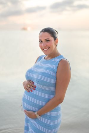 Beachside maternity portrait in blue and white striped dress at sunset.