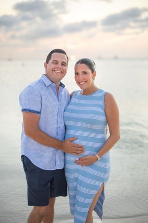 Couple's maternity photo on beach at sunset in coordinating blue outfits.