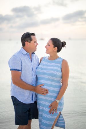 Intimate beach maternity portrait of couple in blue clothing at dusk.
