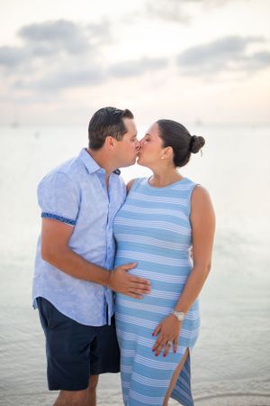 Romantic sunset beach photo of expecting couple sharing a kiss.