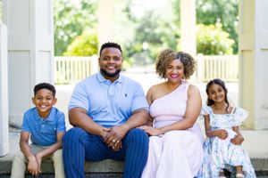 A happy family sitting together on white porch steps on a bright sunny day.