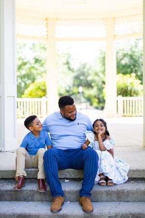 A family of three sits together on stone steps of a covered porch.