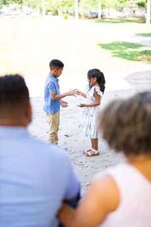 Two children playing together on a pathway while adults watch in the background.