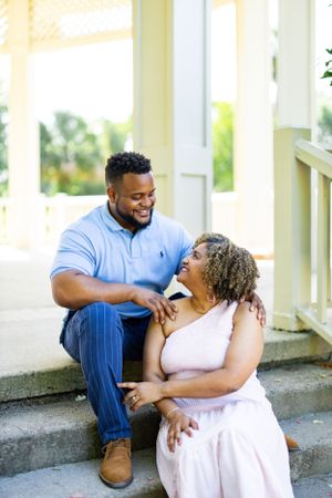 A romantic couple shares a tender moment while sitting on white porch steps.