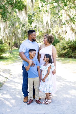 A family of four poses together on a scenic path with Spanish moss draped trees in the background.