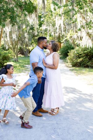 A loving family moment captured outdoors with children playing around their embracing parents.