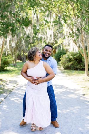 A couple embraces on a sunlit path surrounded by trees with Spanish moss.