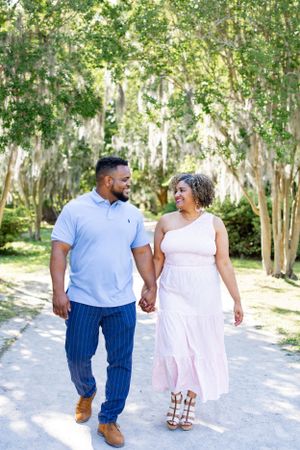 A couple holds hands while walking down a tree-lined path in matching casual outfits.
