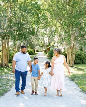A family takes a stroll together on a tree-lined path on a sunny day.