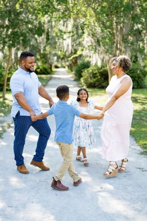 A family dances together on a peaceful garden path surrounded by trees.