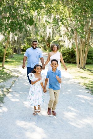 A cheerful family walks together on a tree-lined path during summer.
