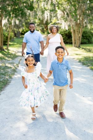 A family walks hand in hand down a sun-dappled garden path.
