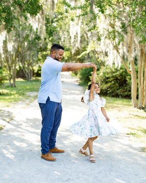 A playful dance moment between two people on a tree-lined path.