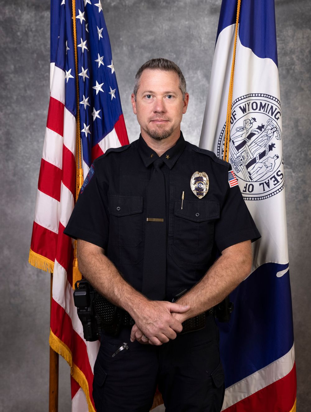 Police officer in uniform standing with American and Wyoming flags in official portrait.