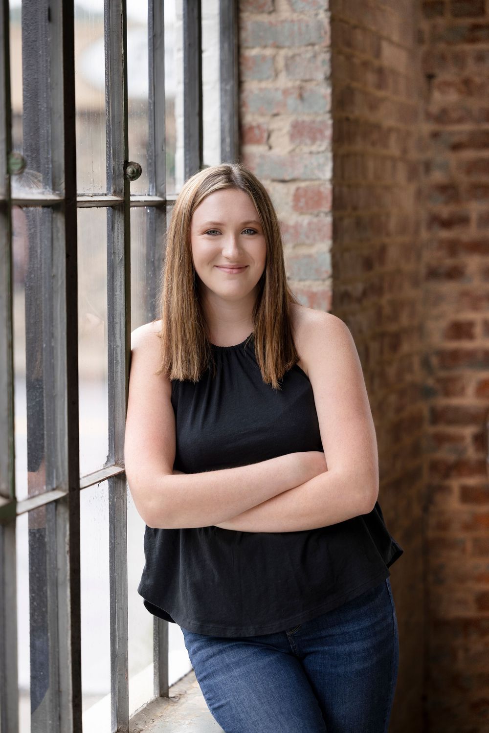 Portrait series of person in black tank top near brick wall with windows.