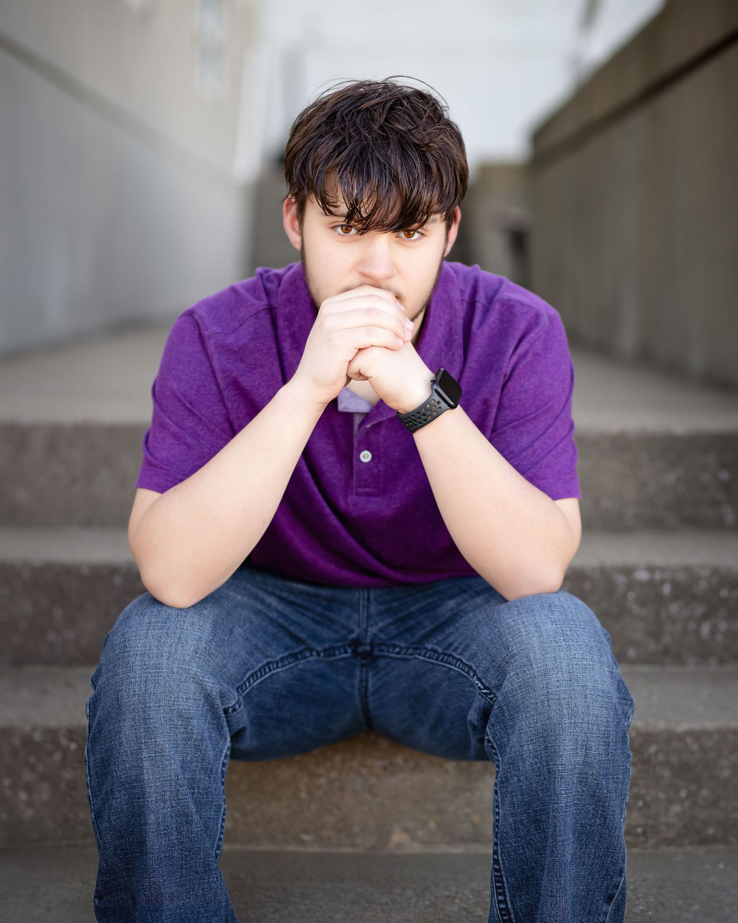 A contemplative figure in a purple polo shirt sits on concrete steps deep in thought.