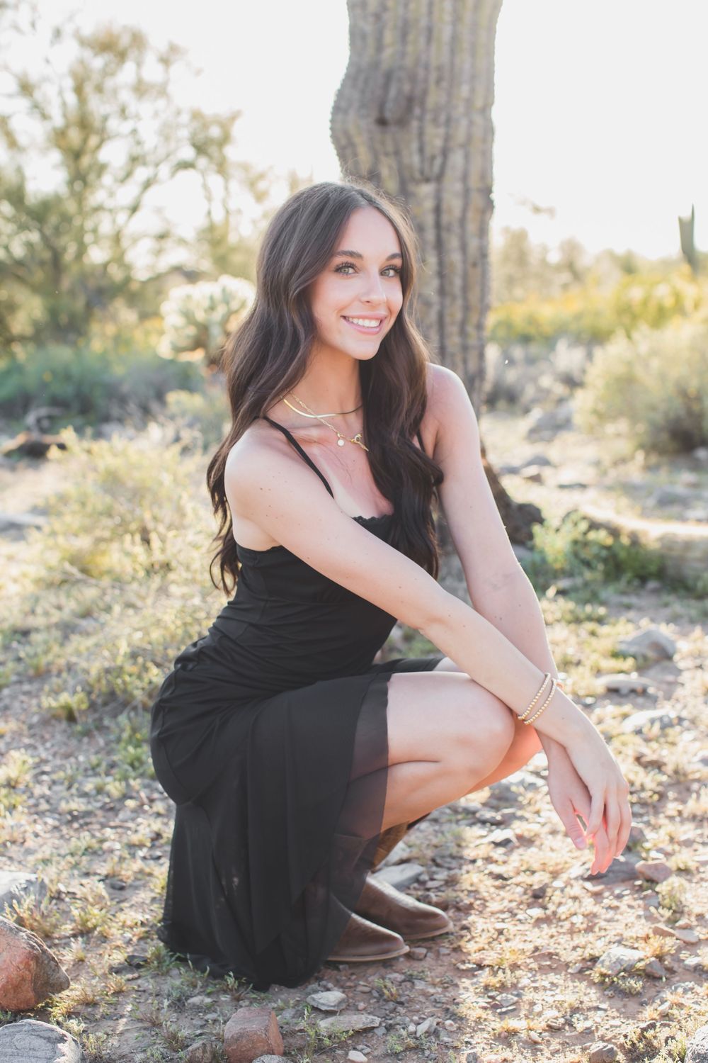 Person in black dress posing in desert landscape with saguaro cactus during golden hour.