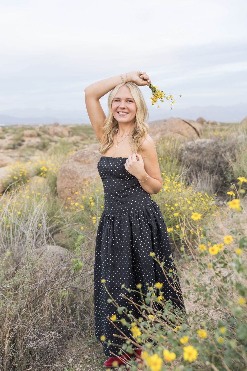 Woman in polka dot dress poses among desert wildflowers during outdoor portrait session.
