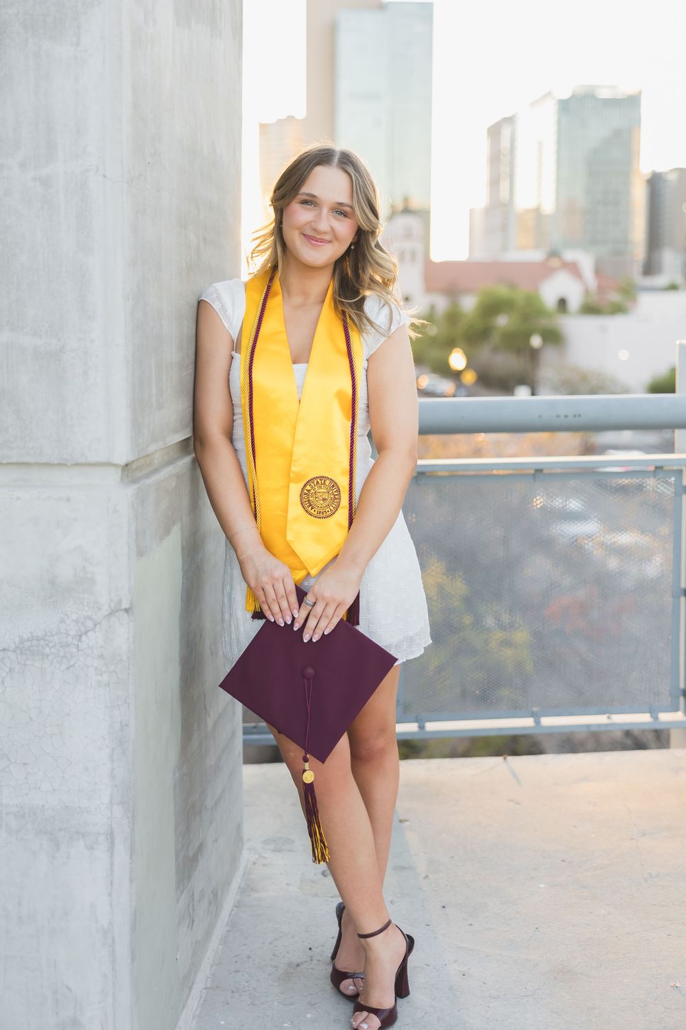 Person in yellow top and maroon dress posing against concrete wall in urban setting.