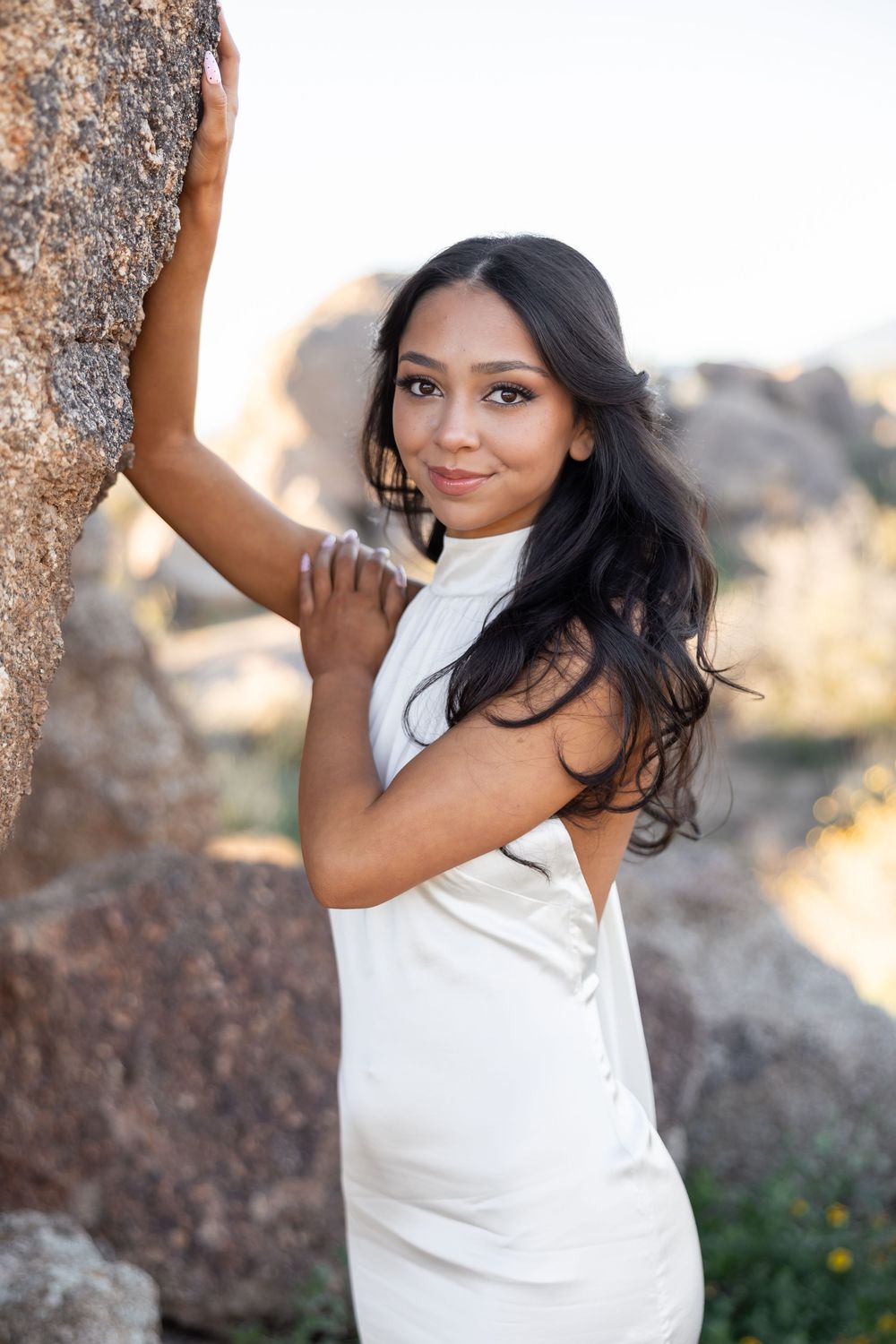Person in white top posing against rocky backdrop in natural outdoor setting.