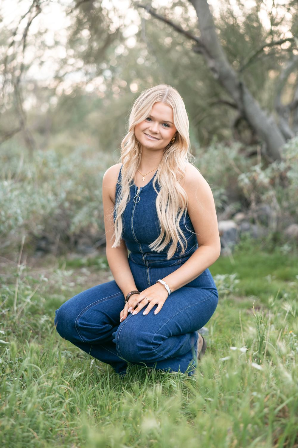 Woman in navy blue jumpsuit poses gracefully on grassy ground during outdoor photoshoot.