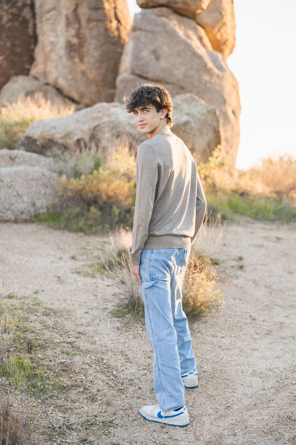 Person in gray shirt and jeans standing near rocky formations in natural outdoor setting.