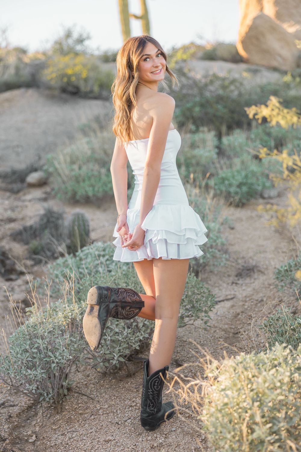 Person in white top posing on desert trail during golden hour photoshoot.