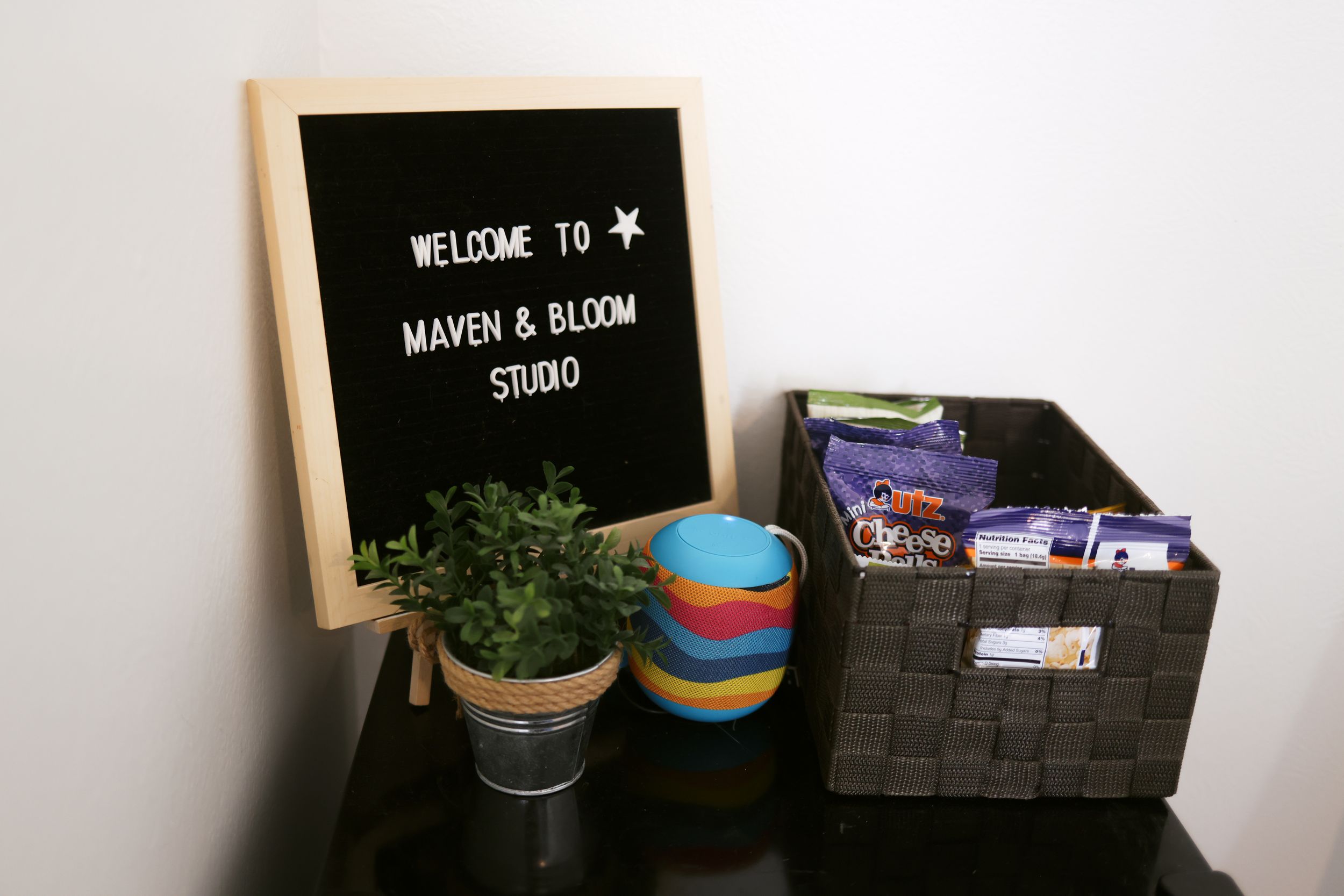 A welcome sign on a letterboard with a potted plant and colorful vase on a dark surface.