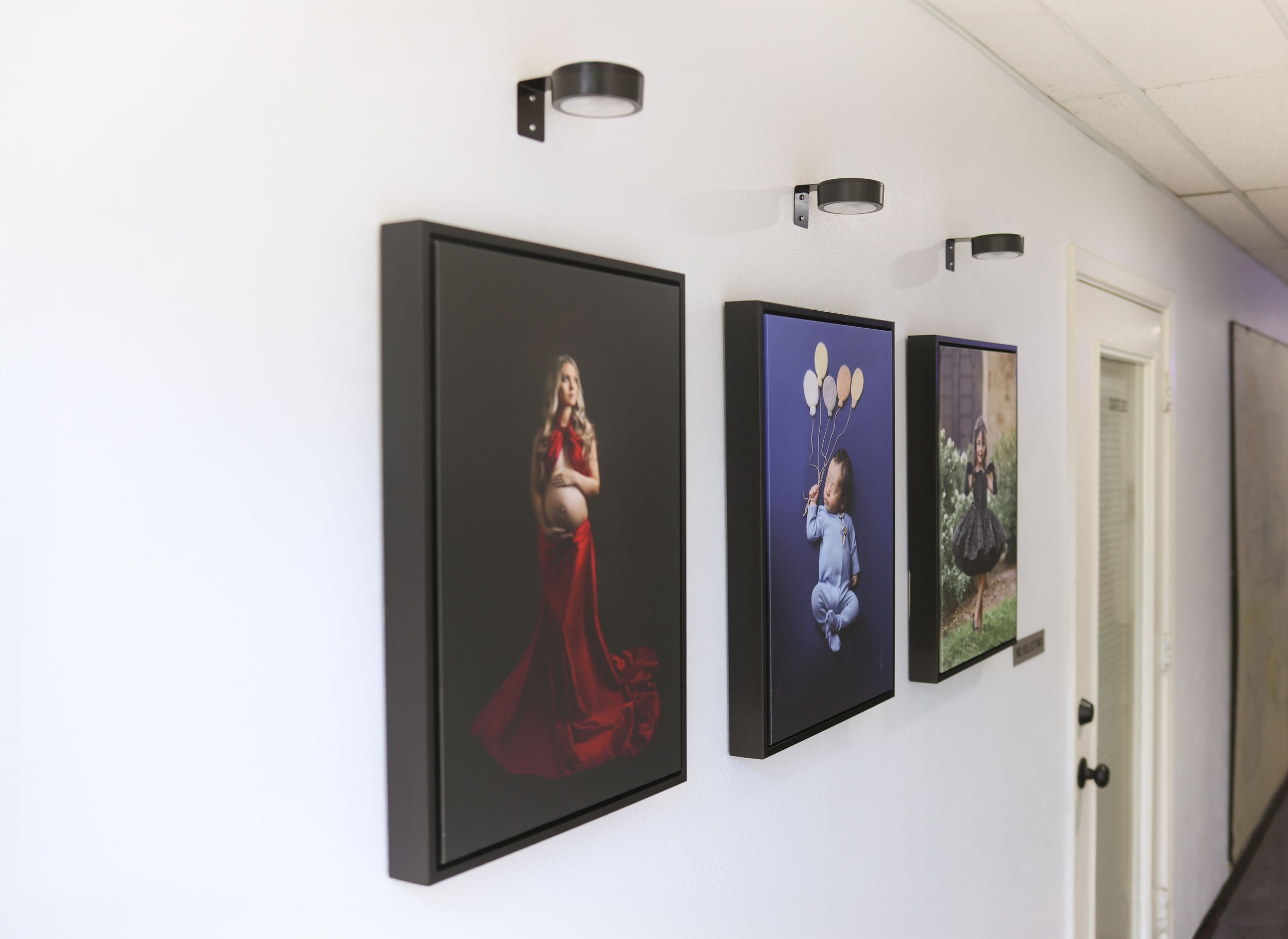 Professional photography studio hallway with large framed portrait prints mounted on a white wall.