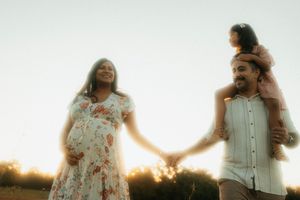 A couple holds hands in a sunlit field at sunset creating a dreamy silhouette against the warm glowing sky.