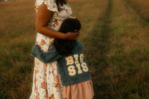 Someone in a floral dress holding a vintage style Big Sis denim shirt against a golden field at sunset.