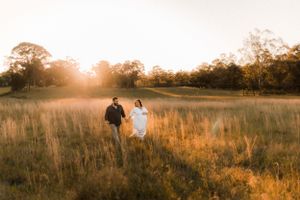 A couple walks through a sun-drenched field at golden hour.