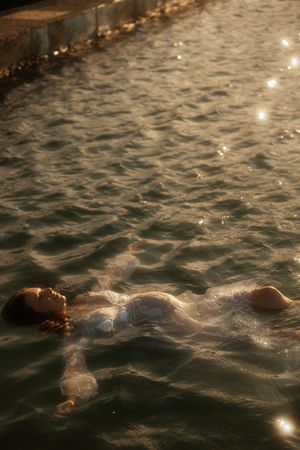 A person floats serenely in shimmering water at dusk with light reflections dancing across the rippling surface.