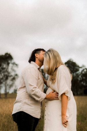 A romantic couple embraces in a golden field during sunset.